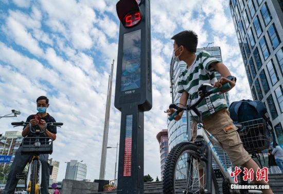 9月15日，位于北京市中关村大街和丹棱街交叉口的智能交通系统吸引路人。近日，一套智能交通系统在此地上线试运行，伴随路口红绿灯的转换，行人通行用的信号灯灯杆会发出语音提示，如有行人闯红灯，系统会发出语音警告，闯灯者的面部会被抓拍，呈现在灯杆的屏幕和路边的大屏幕上。中新社记者